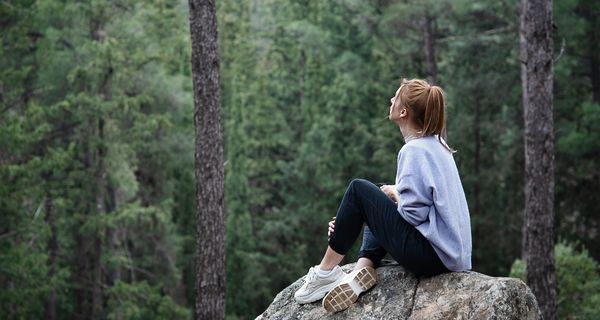 Junge Frau, sitzt auf einem Fels und schaut in den Wald.