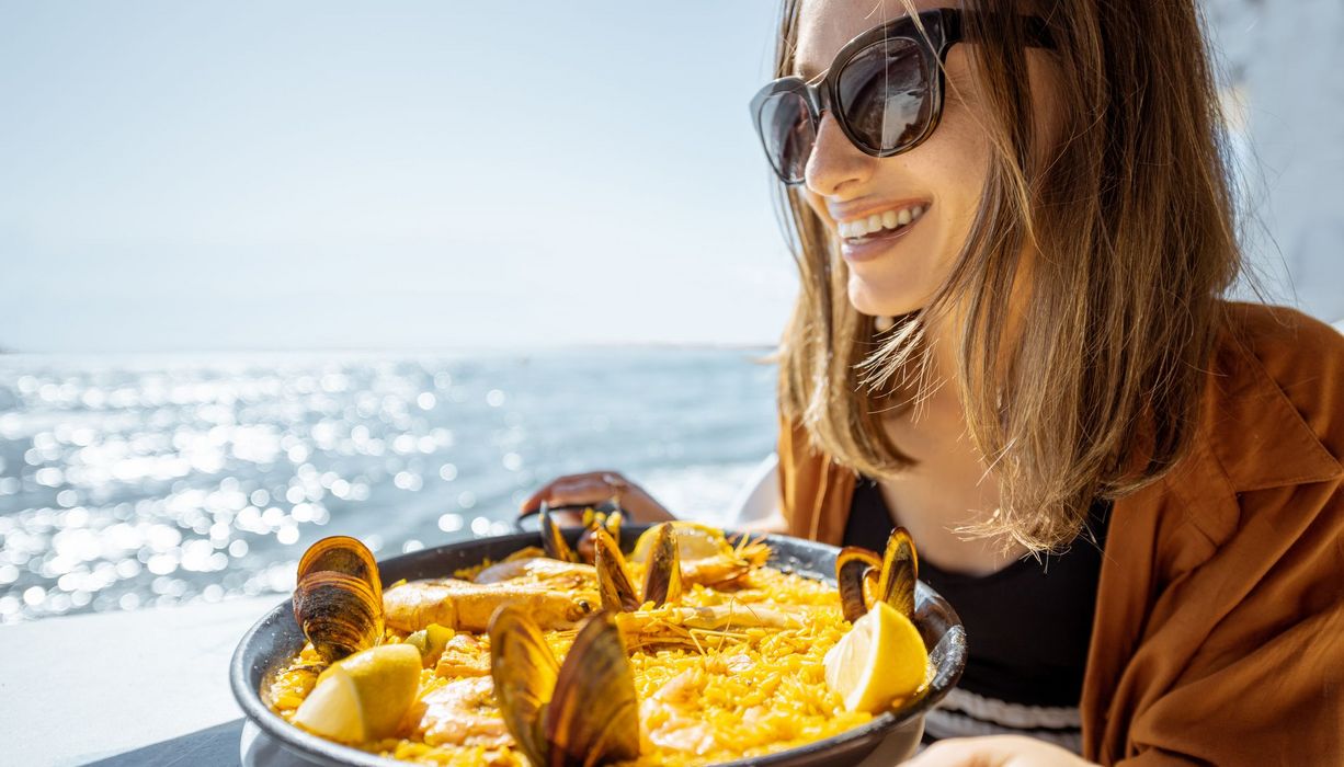 Junge Frau, sitzt am Meer und isst Meeresfrüchte.