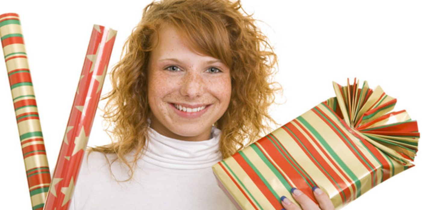 Rothaarige junge Frau mit Geschenkpapier und einem verpackten Geschenk in den Händen