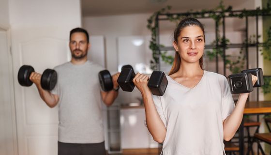 Ein Paar macht Hantelübungen zuhause.