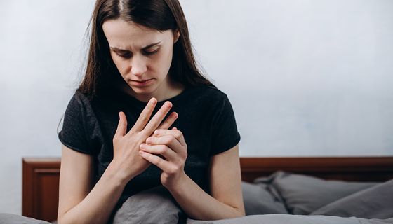 Junges Mädchen, sitzt im Bett und fasst ihre Finger an.