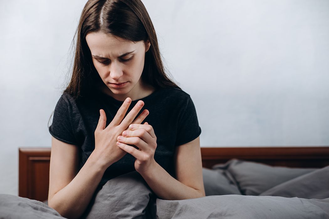 Junges Mädchen, sitzt im Bett und fasst ihre Finger an.