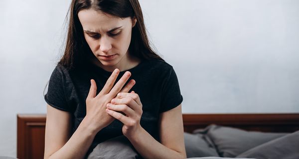 Junges Mädchen, sitzt im Bett und fasst ihre Finger an.