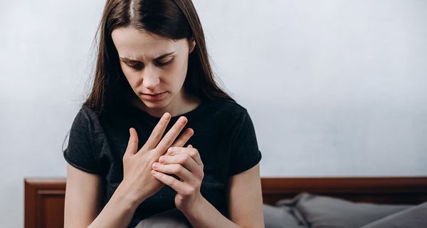 Junges Mädchen, sitzt im Bett und fasst ihre Finger an.