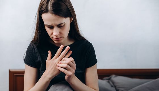 Junges Mädchen, sitzt im Bett und fasst ihre Finger an.