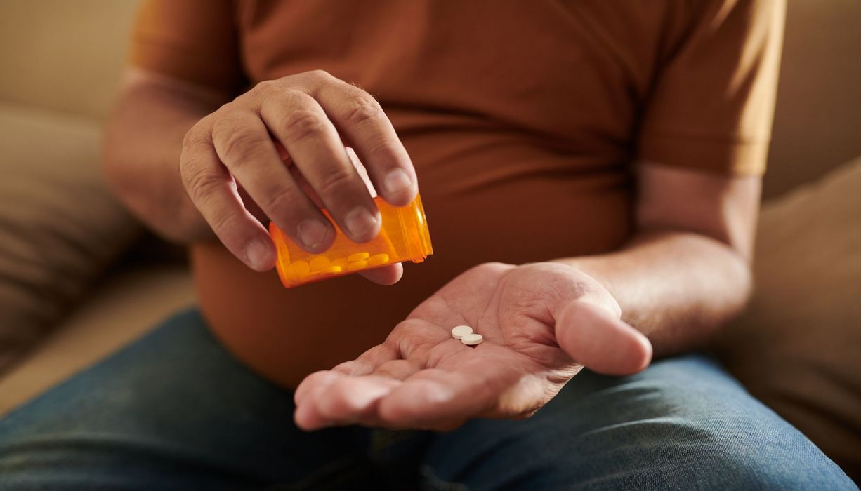 Mann, schüttet aus einer Dose zwei Tabletten in seine Hand.