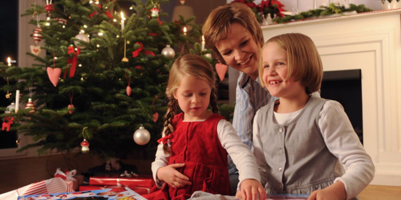 Mutter mit ihren zwei Töchtern bei der Bescherung unterm Weihnachtsbaum