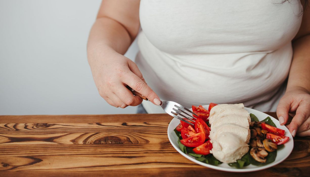 Übergewichtige Frau, isst einen Salat mit Mozzarella.