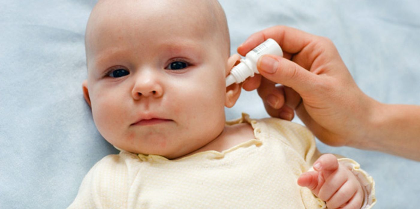 Baby bekommt von einer Hand Tropfen ins Ohr geträufelt