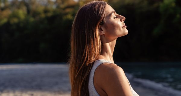Frau, hält ihr Gesicht in die Sonne und lässt sich anstrahlen.