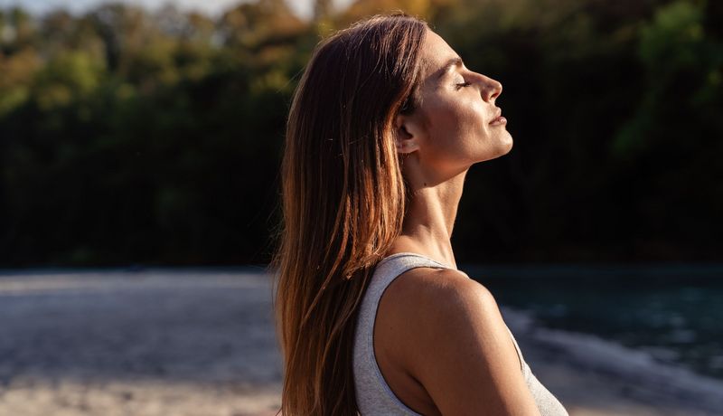 Frau, hält ihr Gesicht in die Sonne und lässt sich anstrahlen.