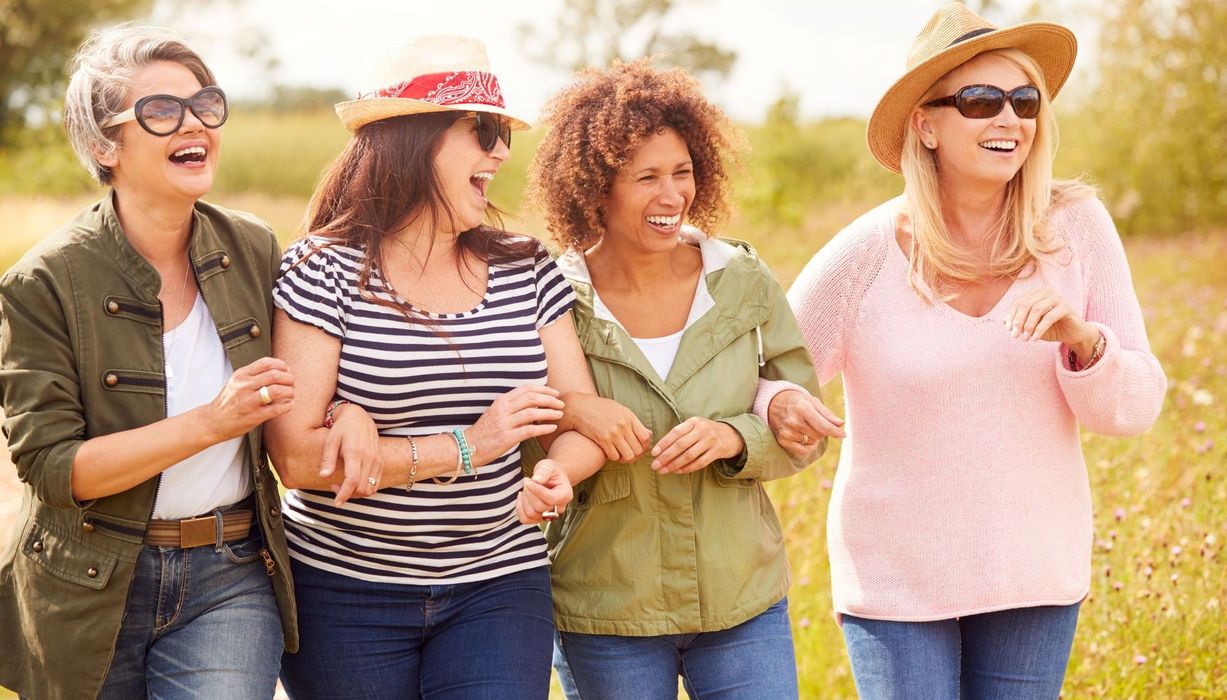 Gruppe von vier lachenden Frauen in der Natur unterwegs.