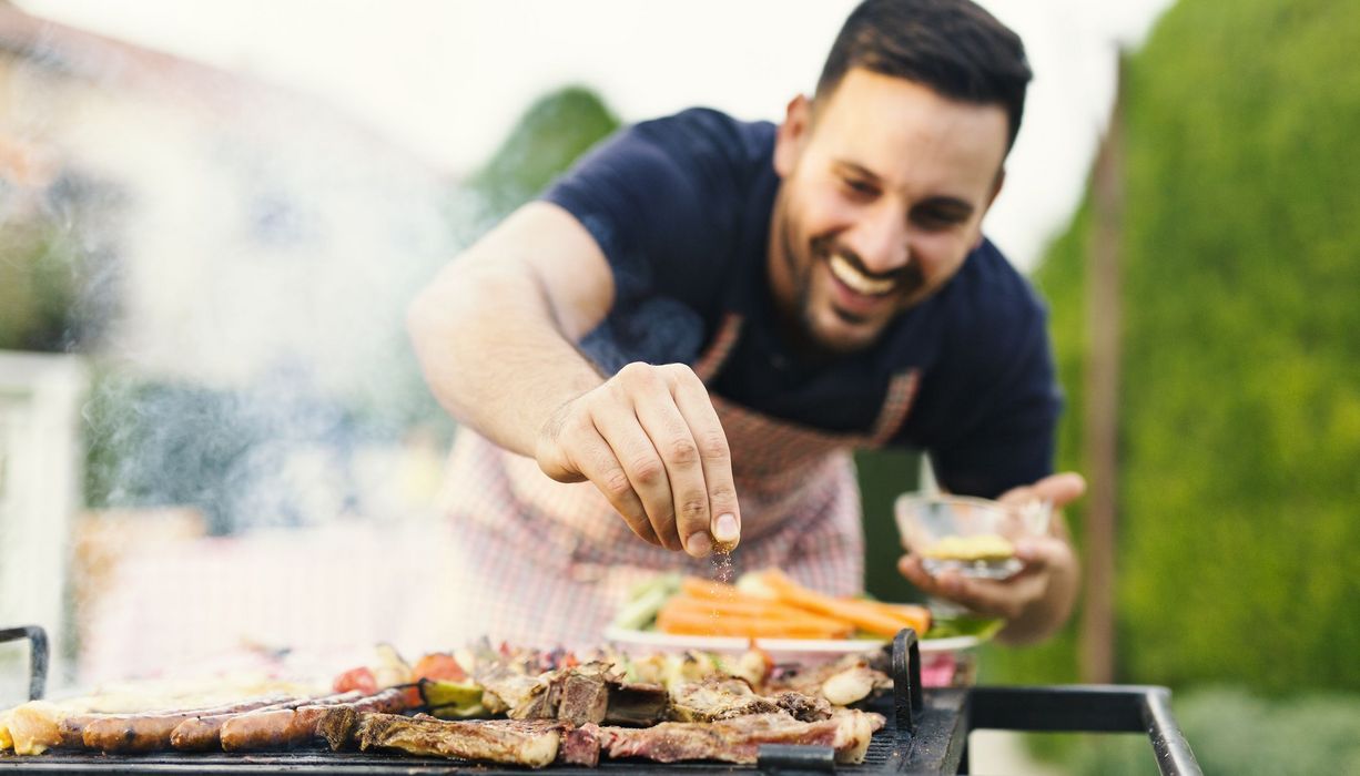 Mann, würzt sein Fleisch auf dem Grill.