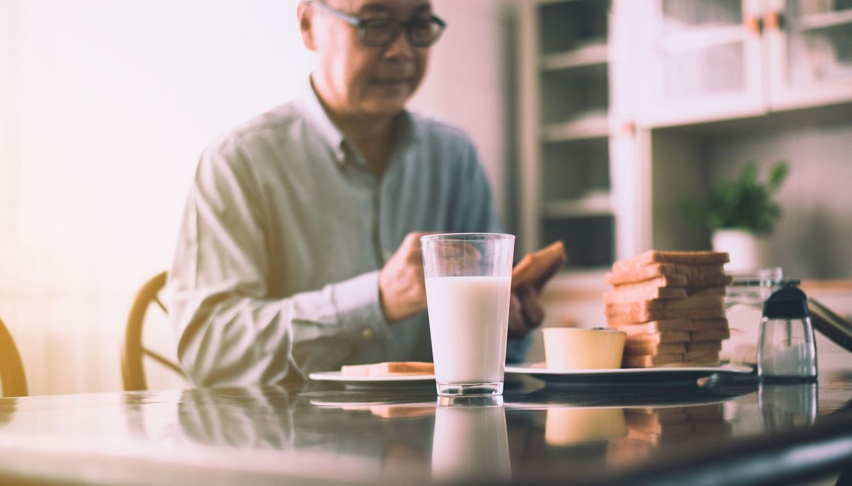 Senior, am Frühstückstisch mit einem Glas Milch.