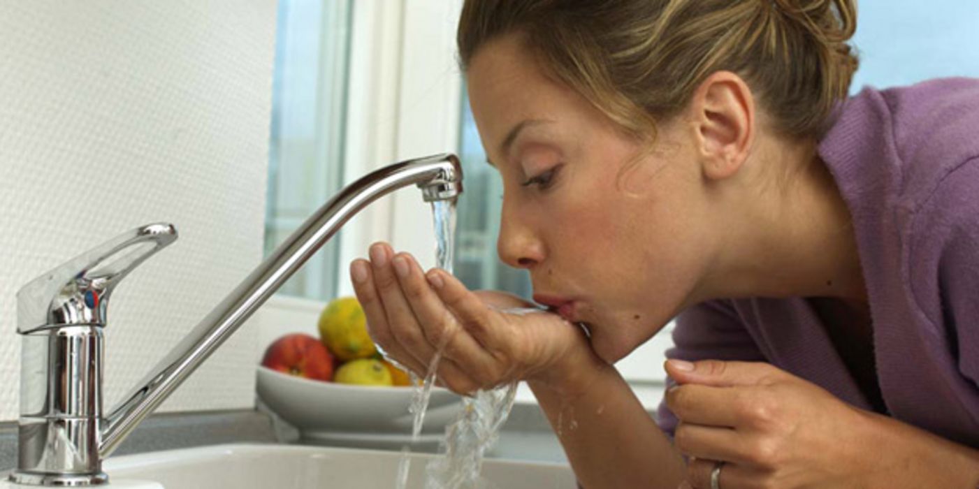 Frau trinkt Wasser aus einem Wasserhahn