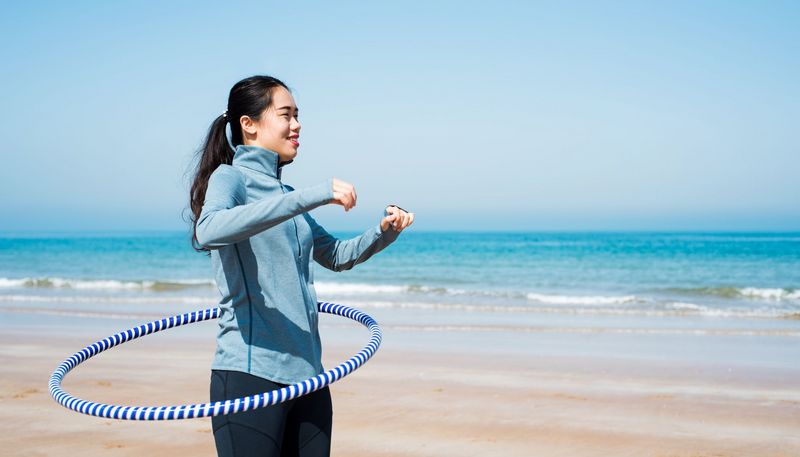 Frau am Strand mit Hula Hoop Reifen.