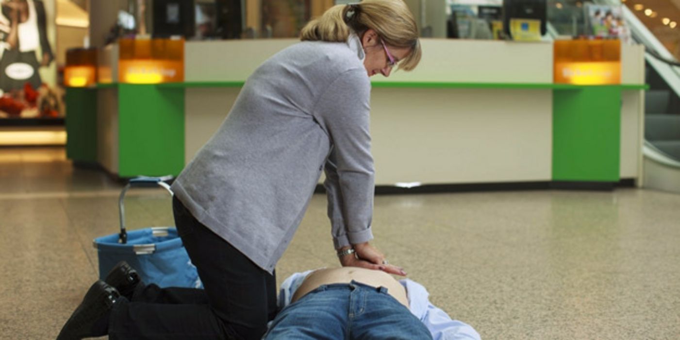 Frau führt Herzdruckmassage bei einem liegenden Mann durch.