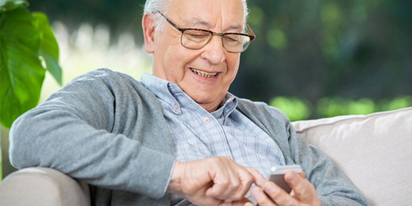 Senior mit Halbglatze auf Couch mit Smartphone