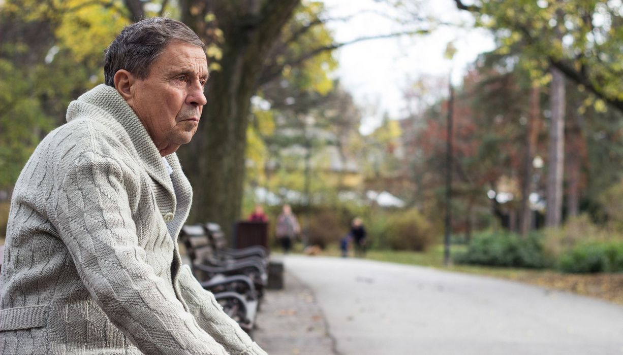 Einsamer Senior sitzt im Park auf einer Bank und starrt in die Ferne.