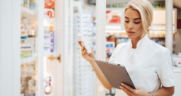 Apothekerin, hält ein Medikament und ein Tablet in der Hand.