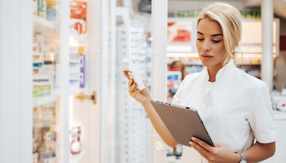 Apothekerin, hält ein Medikament und ein Tablet in der Hand.