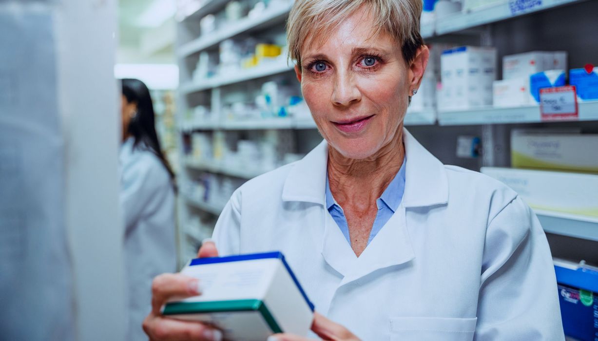 Apothekerin hält ein Medikament in der Hand und schaut ernst in die Kamera.