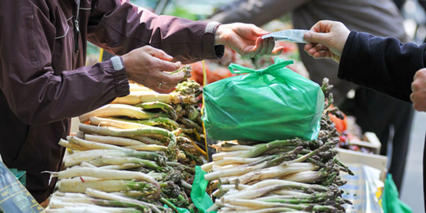 Markstand mit grünem Spargel, grüne Plastiktüte, Geld wird gezahlt von Käufer an Verkäufer, Köpfe sind nicht zu sehen