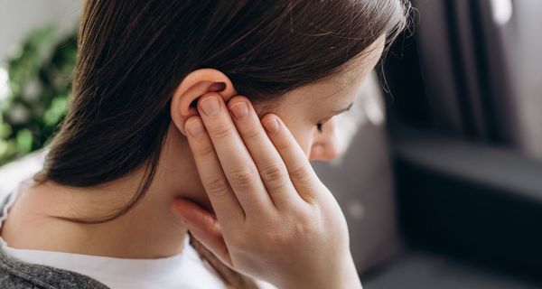 Frau, hält sich eine Hand an das Ohr.