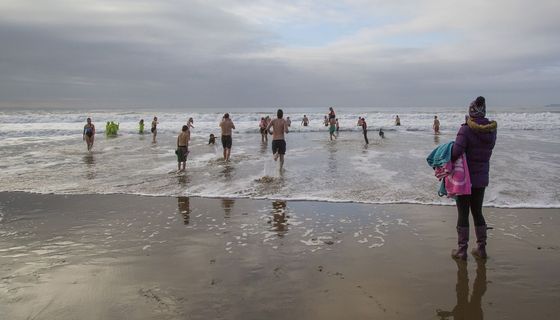Menschen laufen am winterlichen Strand ins Wasser.