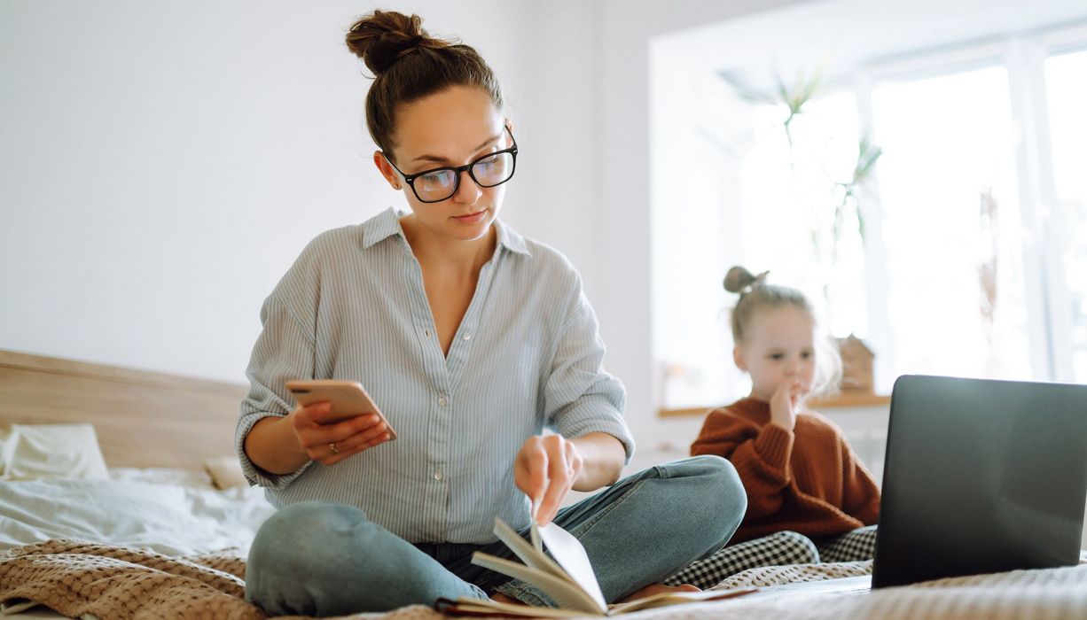 Frau mit Laptop auf dem Bett, neben ihr ihre Tochter.