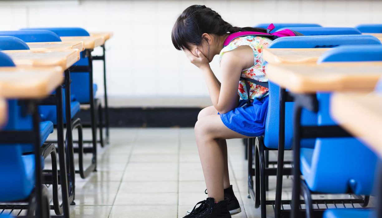 Mädchen, sitzt in der Schule und verbirgt das Gesicht hinter den Händen.