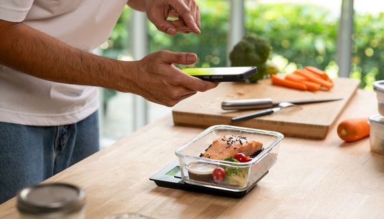 Ein Mann macht in seiner Küche mit seinem Handy ein Foto von seinem Essen.