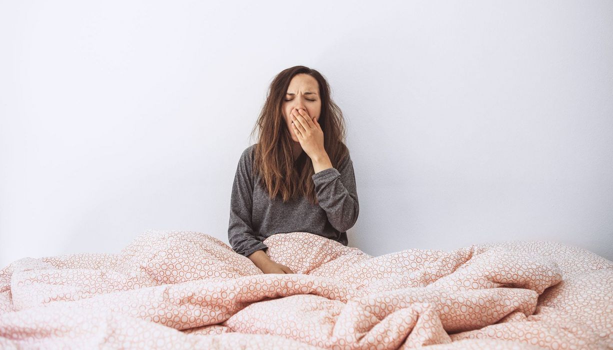 Junge Frau, gähnt, sitzt aufrecht im Bett.