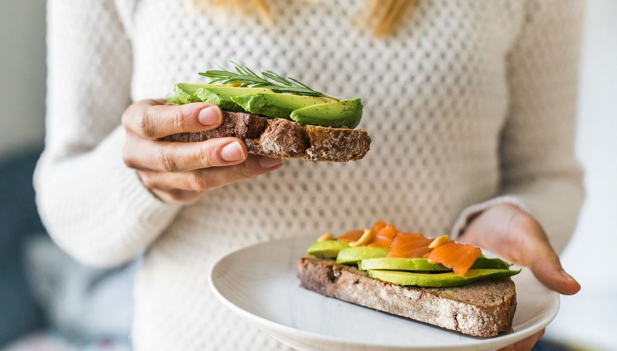 Frau, hat zwei Brote mit Avocado in der Hand.