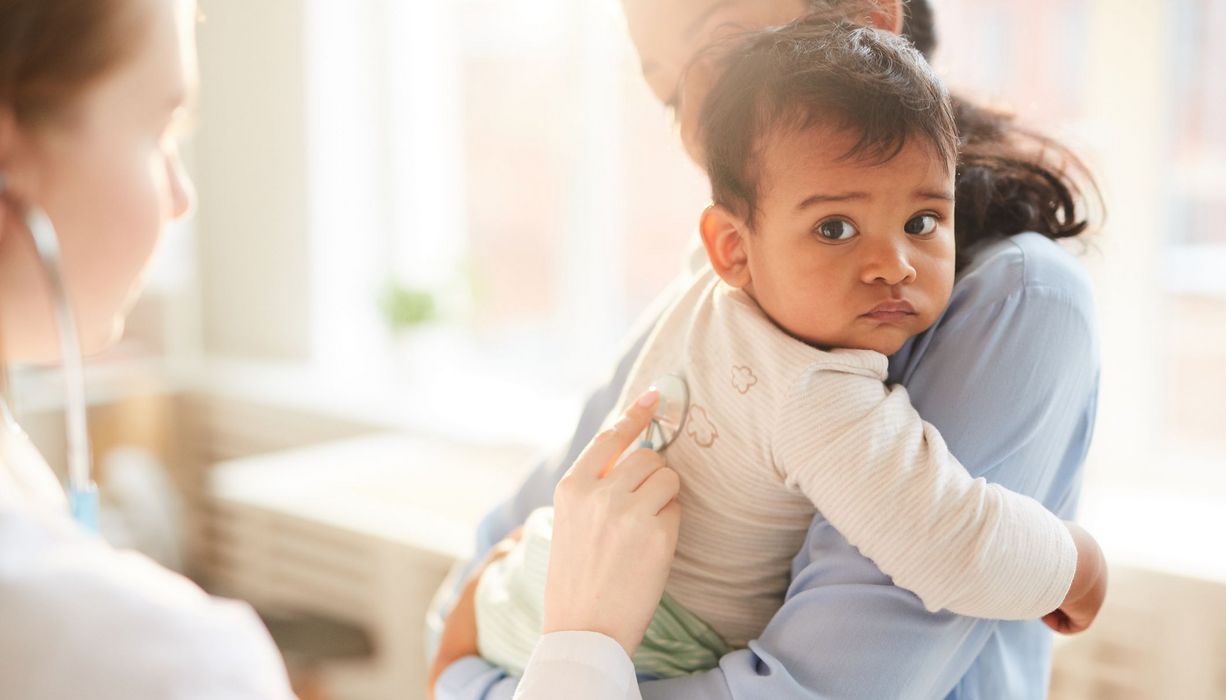 Mutter, hält Baby auf ihrem Arm, wird vom Arzt untersucht.