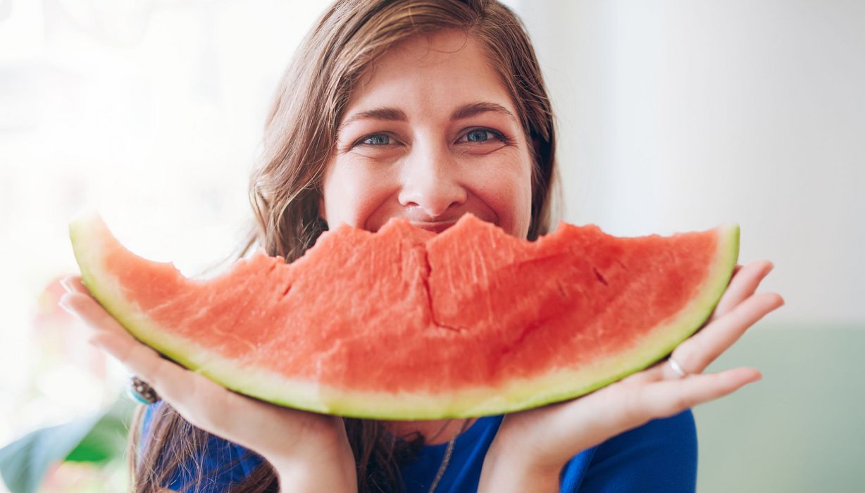 Frau, hält Wassermelone in den Händen und lächelt.