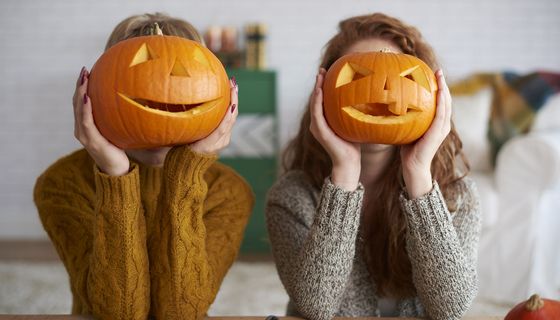 Zwei Frauen, halten sich Kürbisgesichter vor das eigene Gesicht.