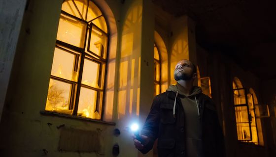 Mann steht mit Taschenlampe in einen alten, unbeleuchteten Haus und guckt zur Decke.
