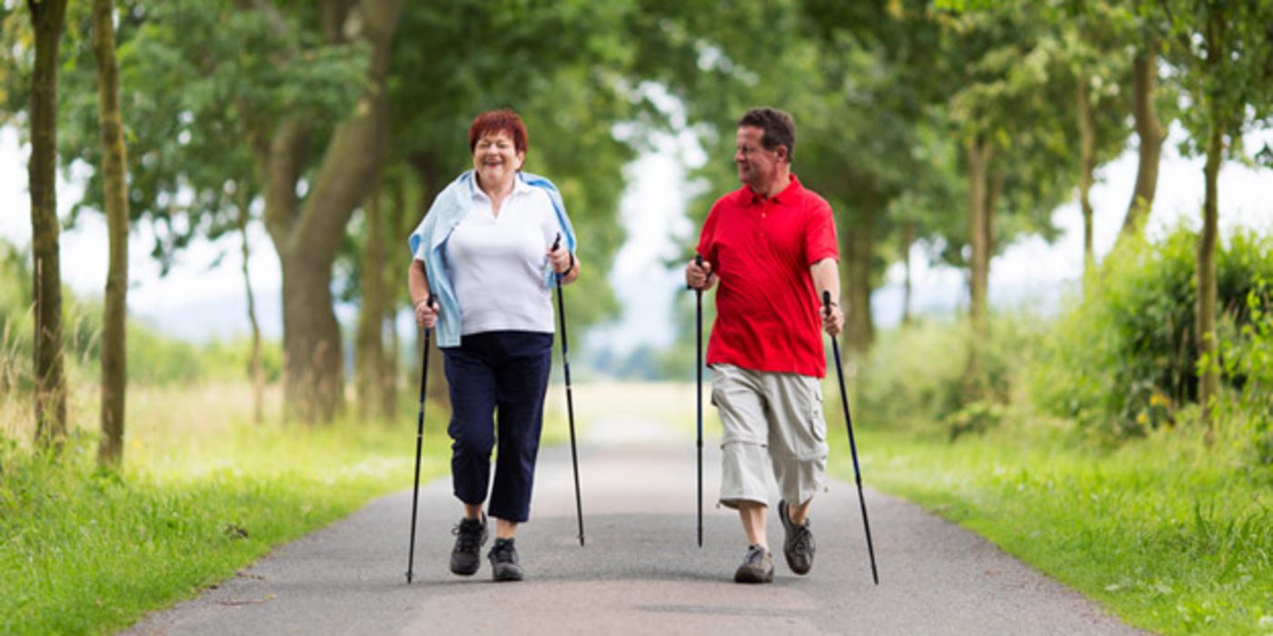 Frau und Mann in mittleren Jahren beim Nordic Walking auf einer Alleestraße