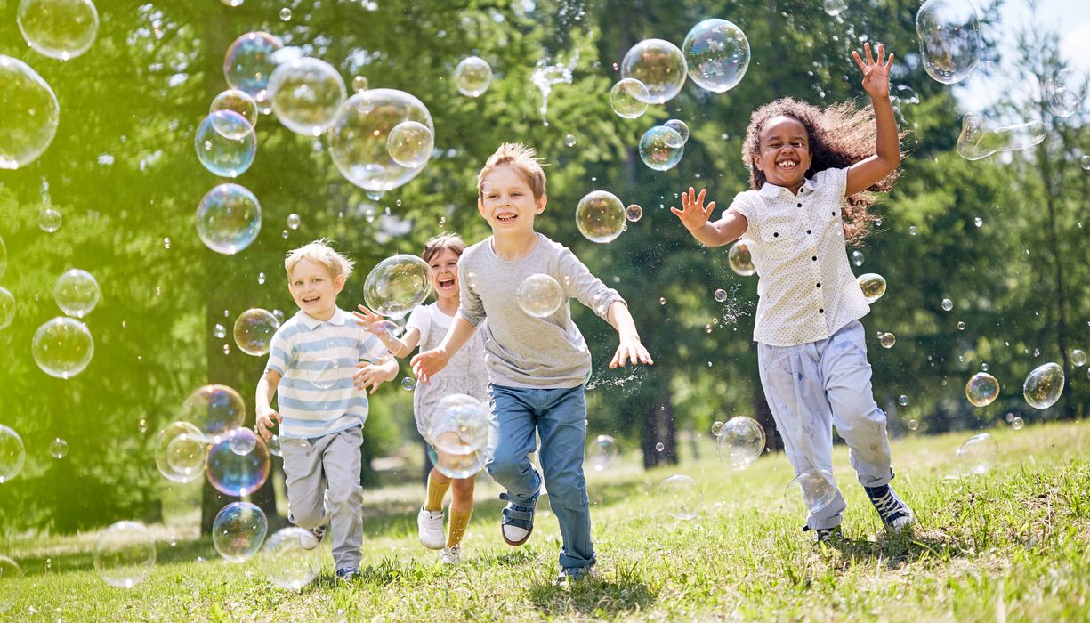 Gruppe von Kindern läuft Seifenblasen hinterher.