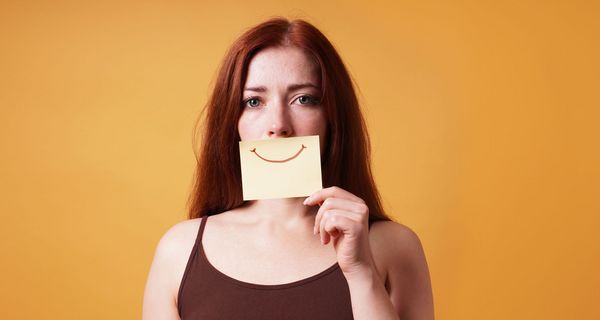 Frau, hält sich ein Blatt mit einem lächelnden Mund vor ihren Mund.