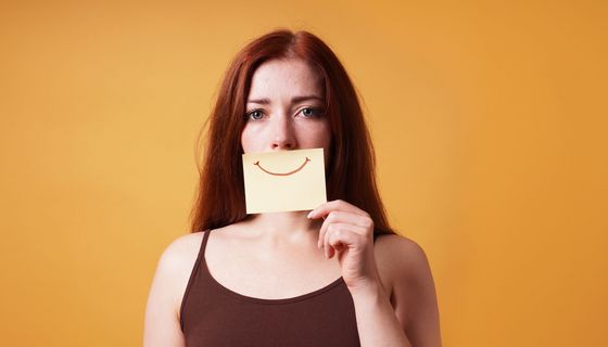 Frau, hält sich ein Blatt mit einem lächelnden Mund vor ihren Mund.