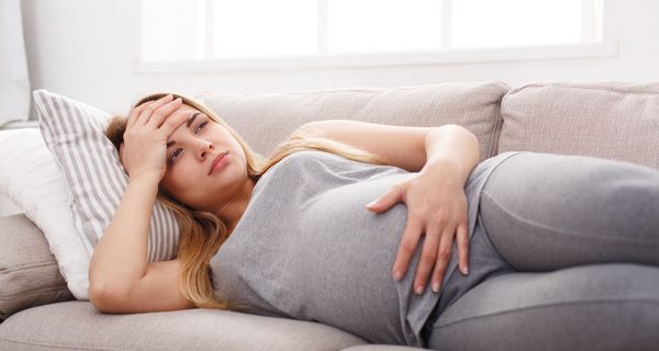 Junge schwangere Frau, liegt mit Kopfschmerzen auf der Couch.