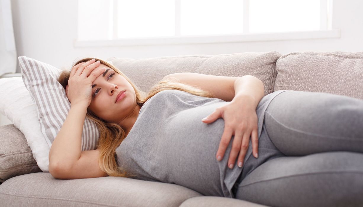 Junge schwangere Frau, liegt mit Kopfschmerzen auf der Couch.