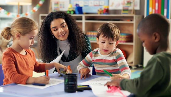 Drei etwa vierjährige Kinder malen unter Aufsicht Bilder.