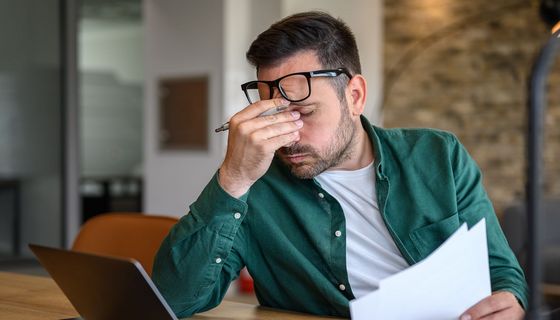 EIn Mann mit Papieren in der Hand reibt sich müde die Augen.