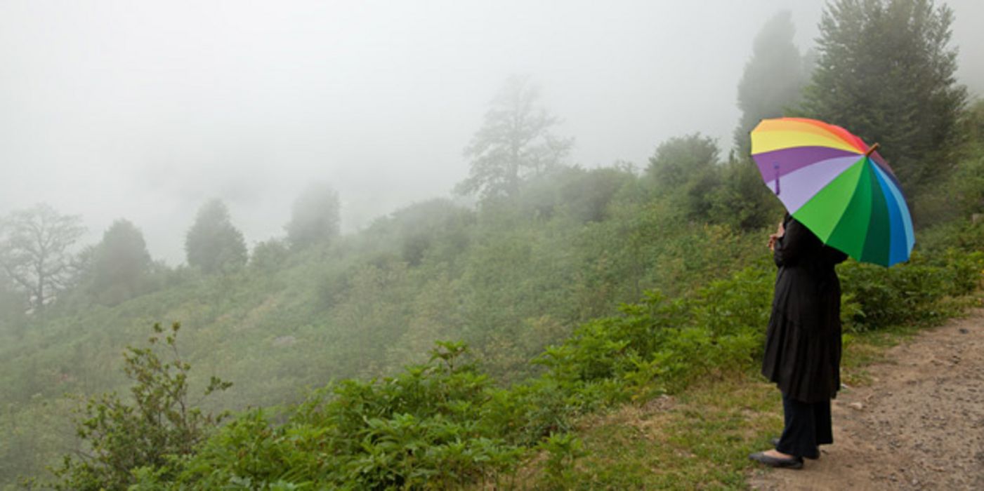 Frau mit buntem Regenschirm steht in nebeliger und hügeliger Landschaft