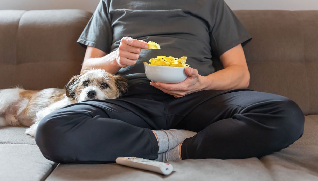 Frau, sitzt auf der Couch und isst Chips.