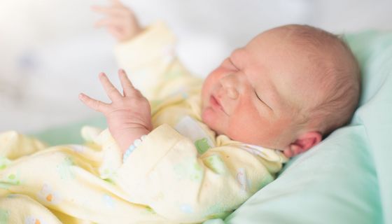 Neugeborenes mit geschlossenen Augen im Krankenhausbett.