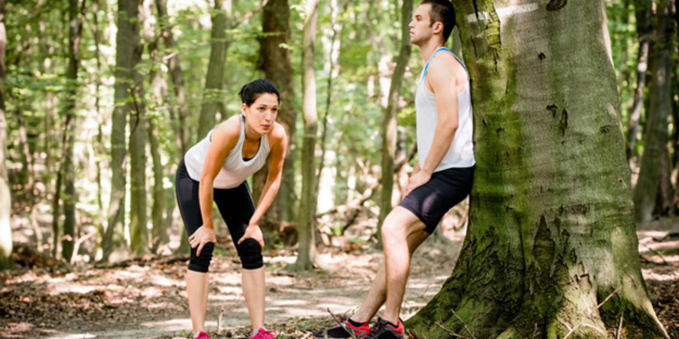 Joggerin und Jogger (ca. Mitte 20) in sommerlicher Sportkleidung verschnaufen im Laubwald